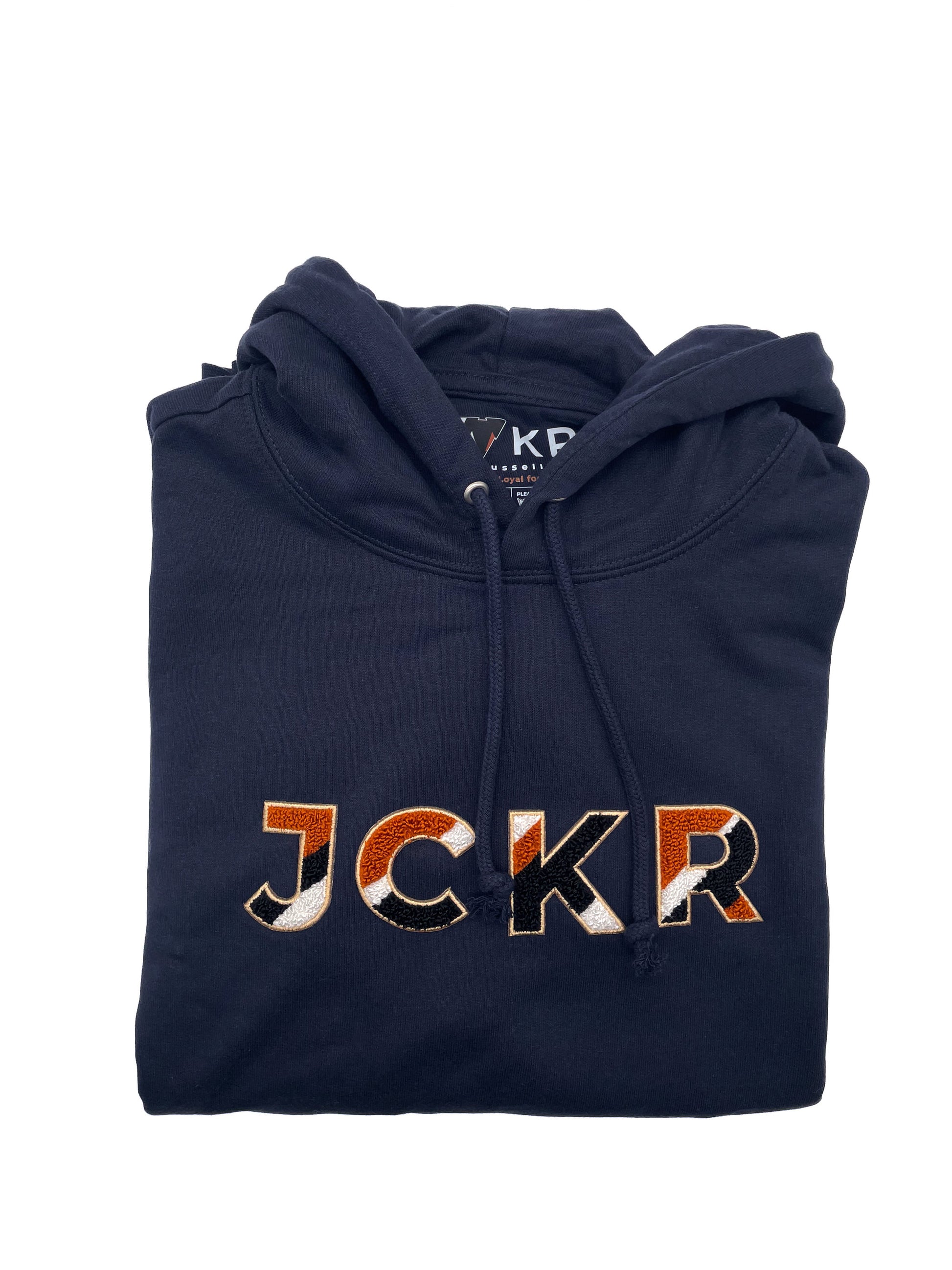 Folded navy blue hoodie with 'JCKR' branding chenille patch on a white background