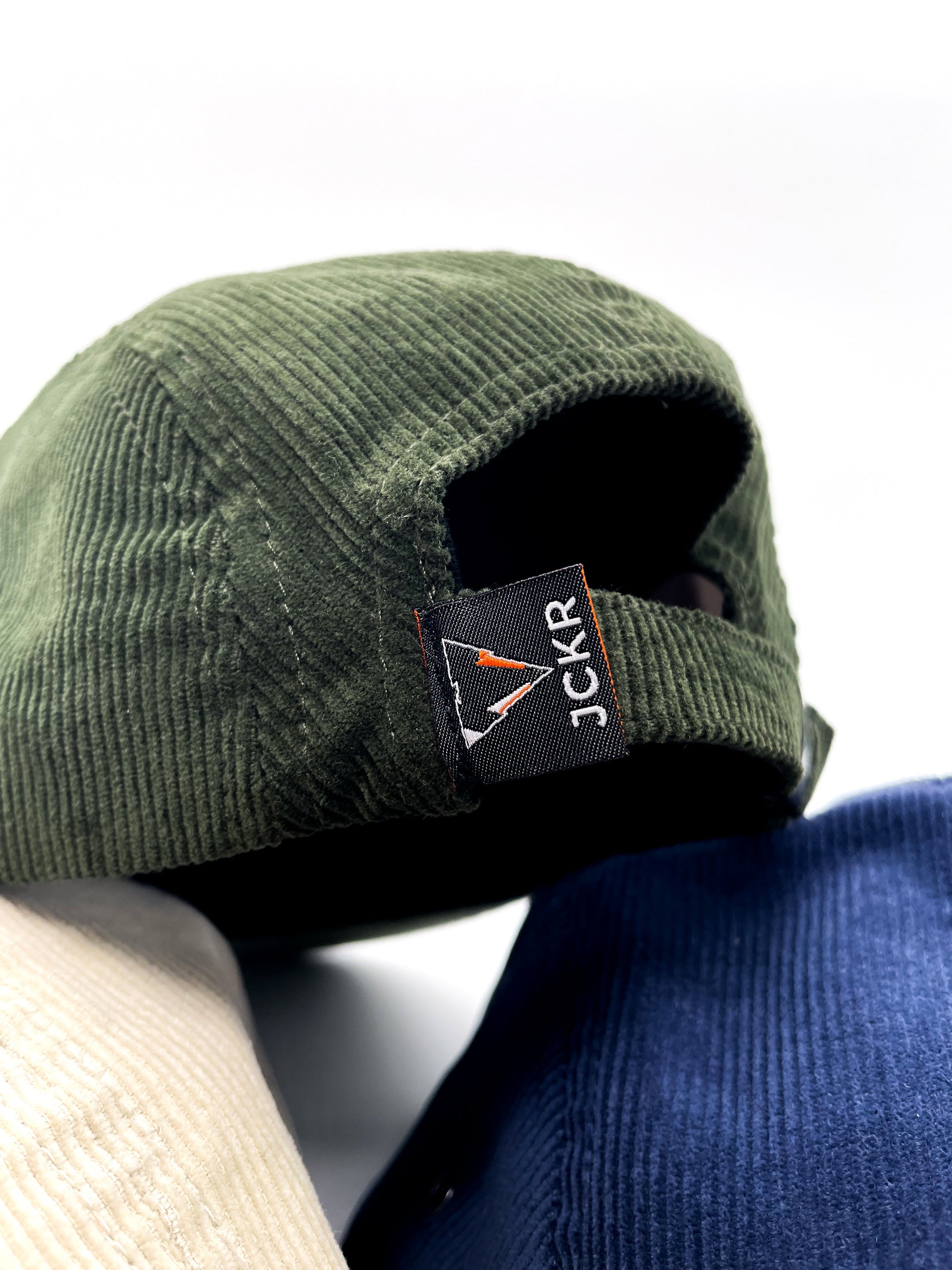 close up of green fine corduroy 5 panels hats with JCKR logo embroidered patch on the front and vowen laben on the back