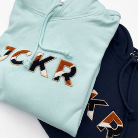 Glacial blue and navy blue hoodies with JCKR chenille patch on the front, on a white background