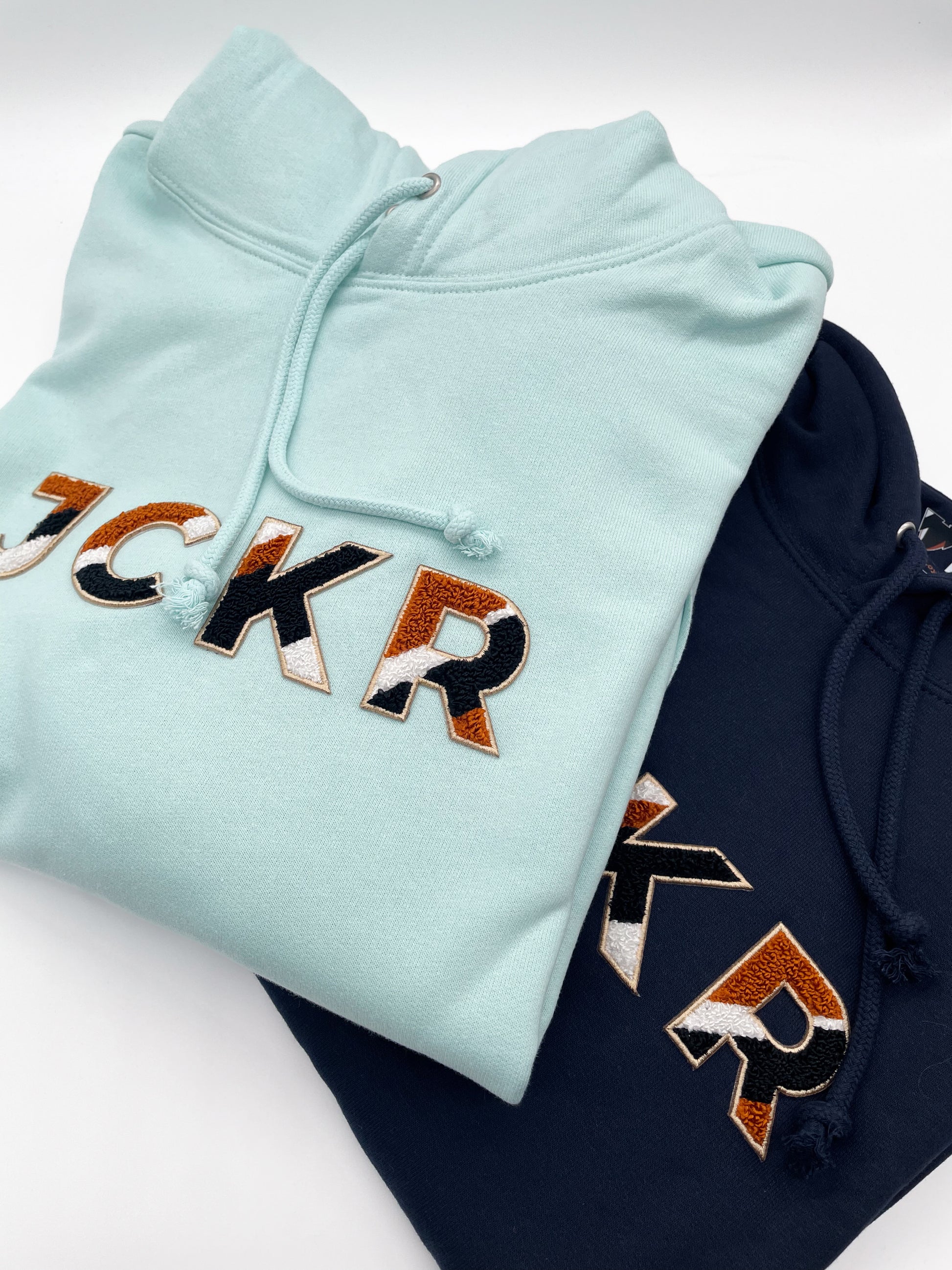 Glacial blue and navy blue hoodies with JCKR chenille patch on the front, on a white background