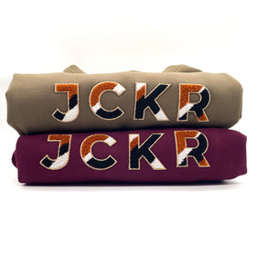 Two folded hoodies with JCKR chenille ptach design on the front, on a white background