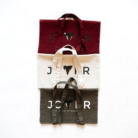 Four tote bags in red, beige, black, and white with a printed JCKR logo on a white background.
