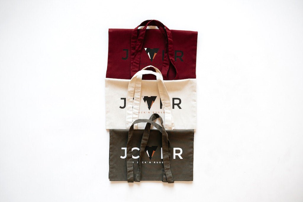 Four tote bags in red, beige, black, and white with a printed JCKR logo on a white background.