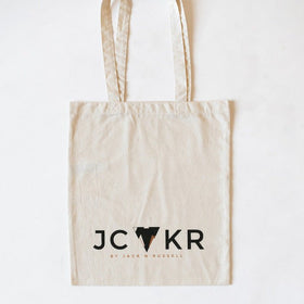 Beige tote bag with 'JCKR' printed logo on a white background