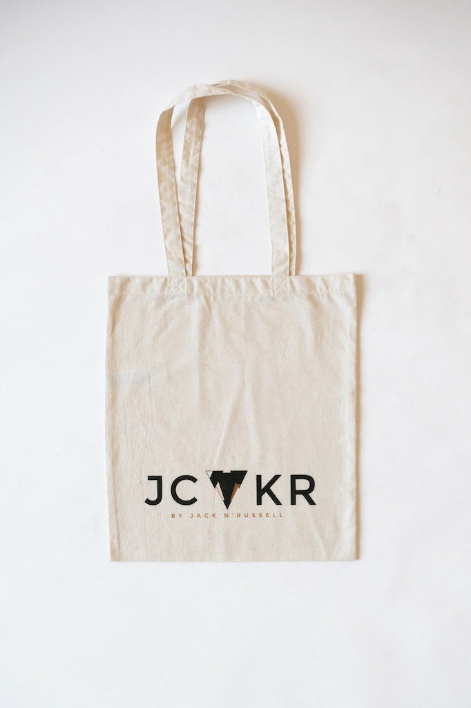 Beige tote bag with 'JCKR' printed logo on a white background