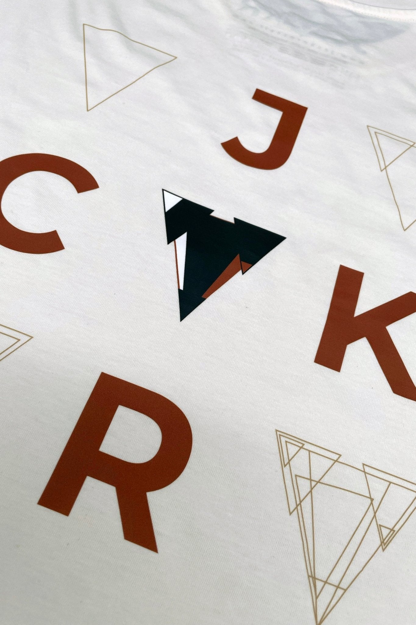 White loose fit JCKR t-shirt with brown letters and geometric shapes on a white background