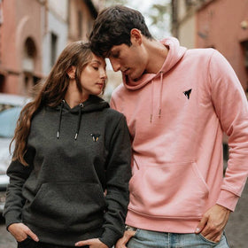 Two people wearing matching JCKR hoodies on a street : one pink and a dark heather grey with embroidered logo 