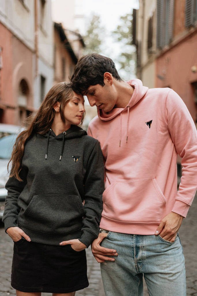 Two people wearing matching JCKR hoodies on a street : one pink and a dark heather grey with embroidered logo 