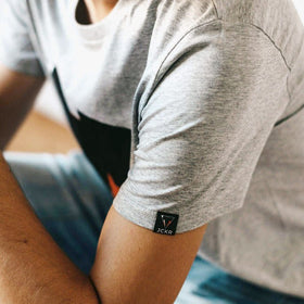 Person wearing the JUNE organic cotton gray t-shirt with a brand logo on the sleeve from JCKR