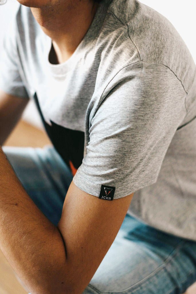 Person wearing the JUNE organic cotton gray t-shirt with a brand logo on the sleeve from JCKR