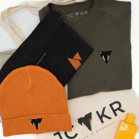 Collection of JCKR branded clothing and accessories and sweater on a white background