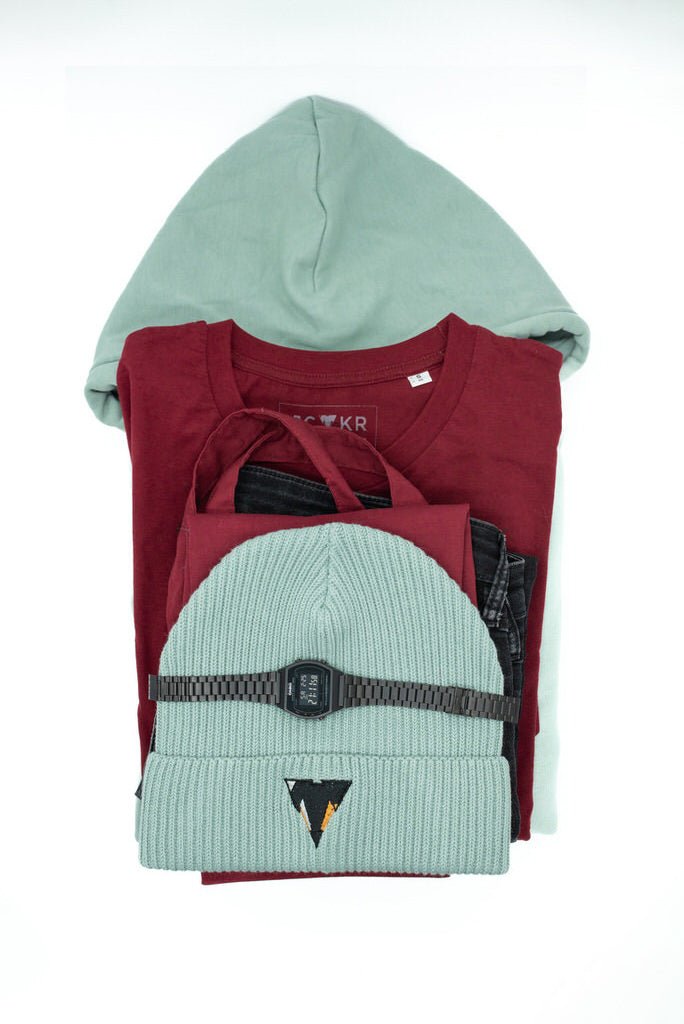 Stack of folded clothes including a bordeaux t-shirt, aloe green JCKR hoodie, and aloe green beanie from JCKR Clothing