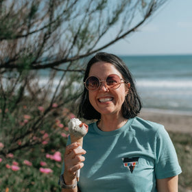 Woman holding an ice cream cone by a beach wearing a SUMMER JCKR organic cotton t-shirt with ocean and sky in the background