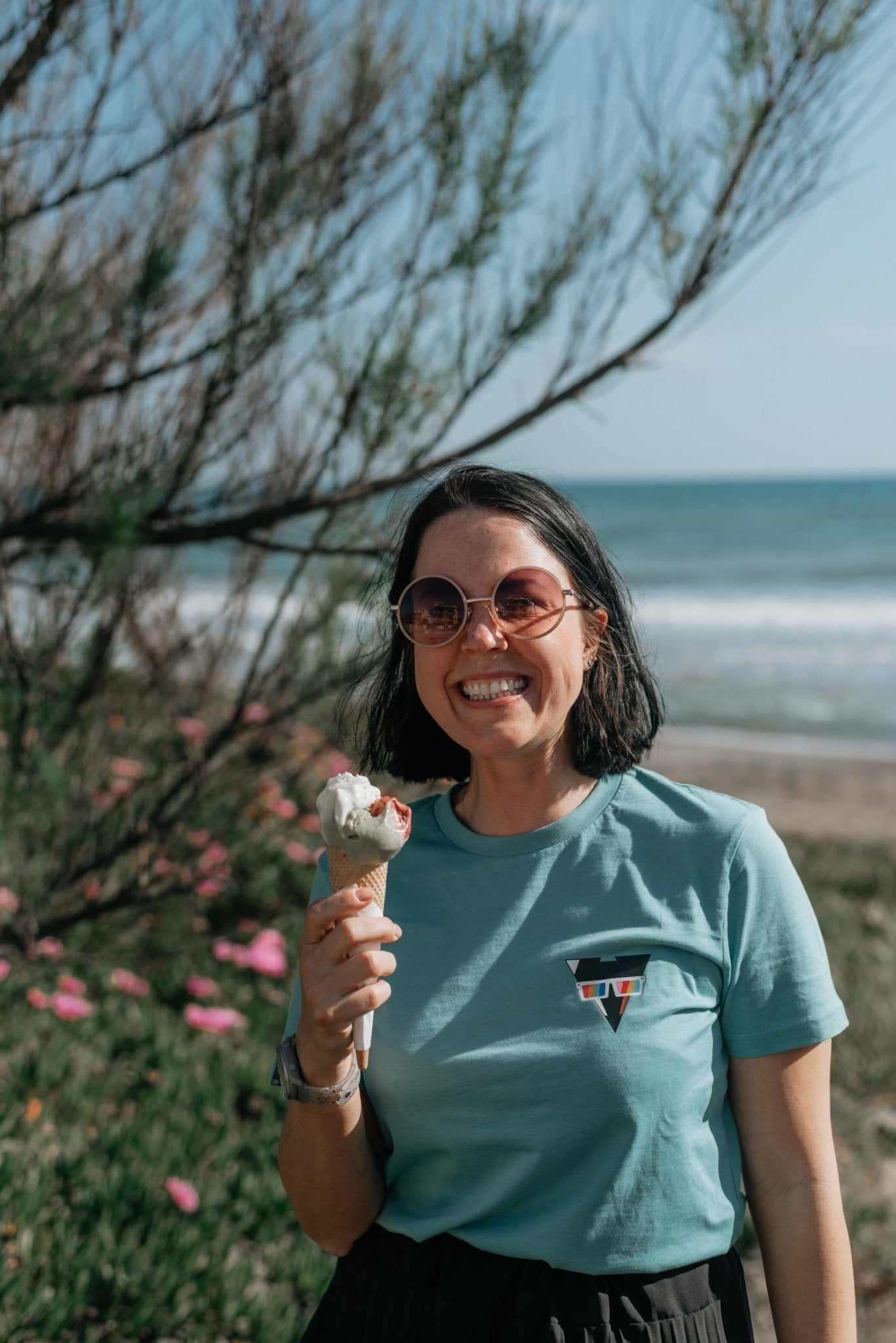 Woman holding an ice cream cone by a beach wearing a SUMMER JCKR organic cotton t-shirt with ocean and sky in the background